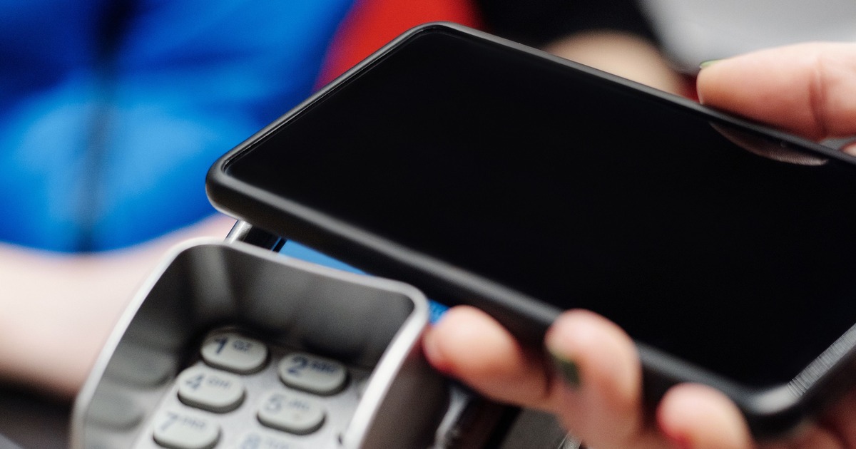 Una mano sostiene un teléfono con la pantalla negra junto a un terminal de pago con teclado